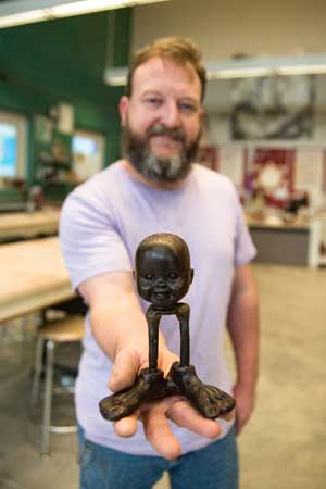 Nelson Grice holds a piece that is the "core" of a larger sculpture. This is an example of a work in progress featuring a baby face, a symbol of the child at the core of his work. 